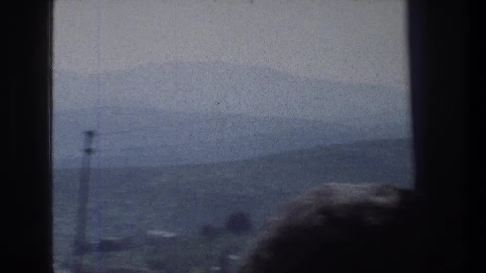 Window-framed 1976 Jerusalem overlook with a tall pole, blue-gray haze, distant hills, and a partial silhouetted head in front.