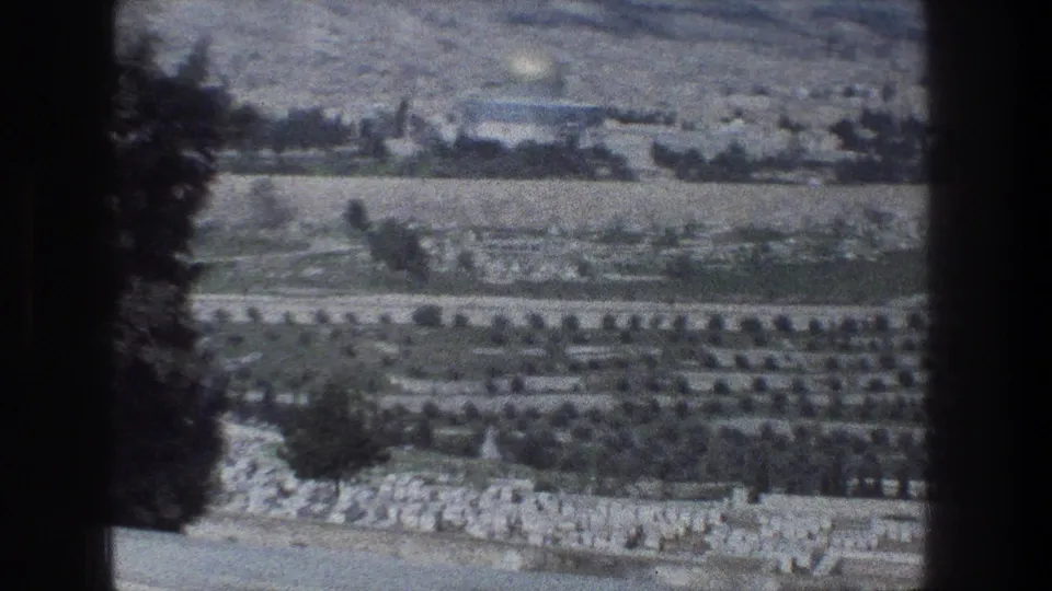 A 1976 Jerusalem landscape frame shows olive-grove-like rows, stone walls, fields, and scattered buildings on hazy hills.