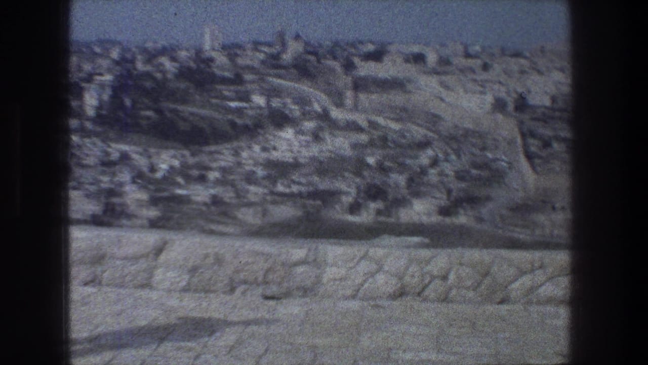 1976 8mm view over Jerusalem from a stone-walled overlook, with dense buildings and roads under a hazy sky.