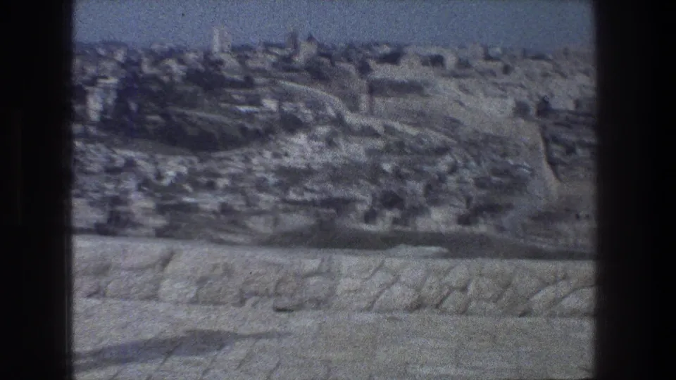1976 8mm view over Jerusalem from a stone-walled overlook, with dense buildings and roads under a hazy sky.