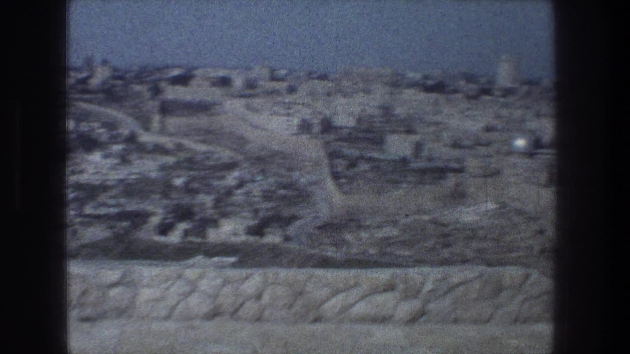 Soft 8mm view over stone parapet toward pale buildings and walls under blue sky.