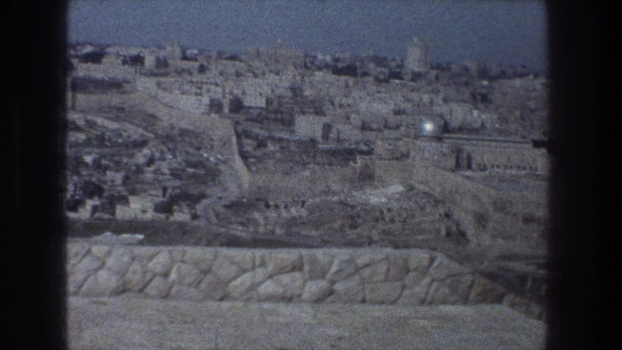 1976 Jerusalem frame with a clearer panoramic view of pale stone buildings, old walls, roads or terraces, and a foreground parapet.
