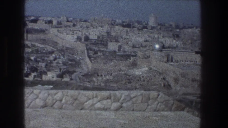 1976 Jerusalem frame with a clearer panoramic view of pale stone buildings, old walls, roads or terraces, and a foreground parapet.