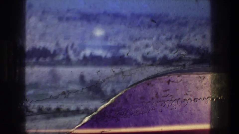 Faded 8mm frame from Jerusalem, with a distant bright dome, low city forms, dark trees, and visible scratches or emulsion marks in the foreground.