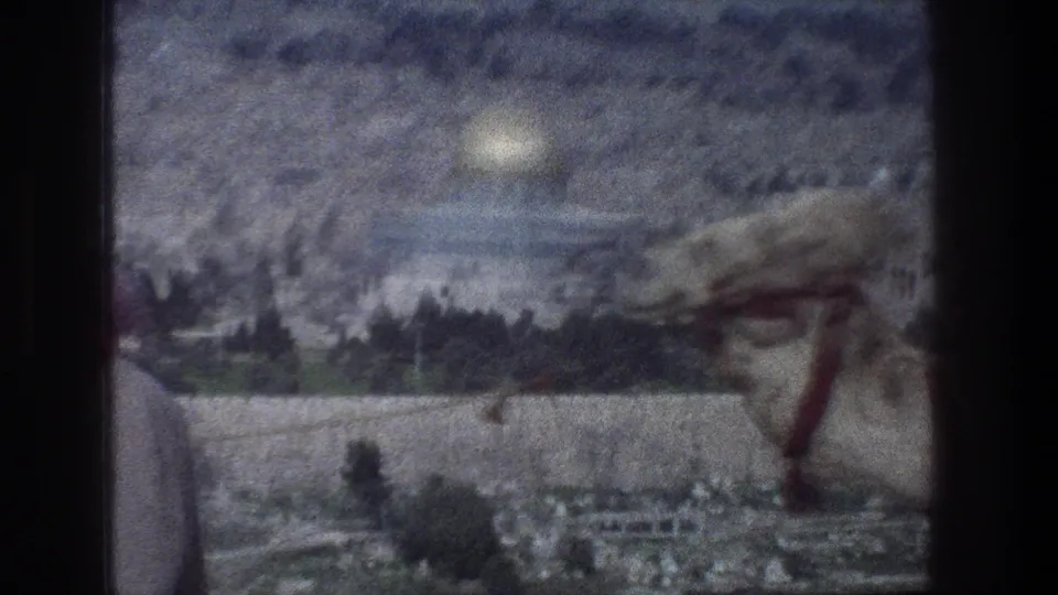 Soft 1976 8mm frame of a camel passing across a Jerusalem panorama with the Dome of the Rock behind it.