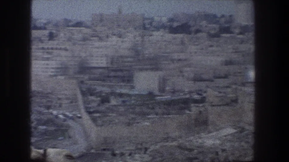 Soft 8mm aerial view over Jerusalem with terraced buildings, road lines, distant blocks, and dark film borders.