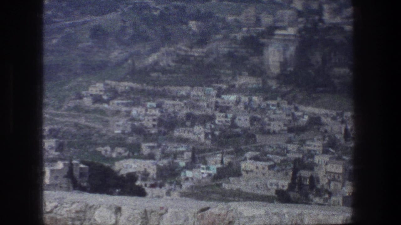 Elevated 1976 Jerusalem view showing dense hillside buildings, roads, and barren slopes in soft 8mm color.