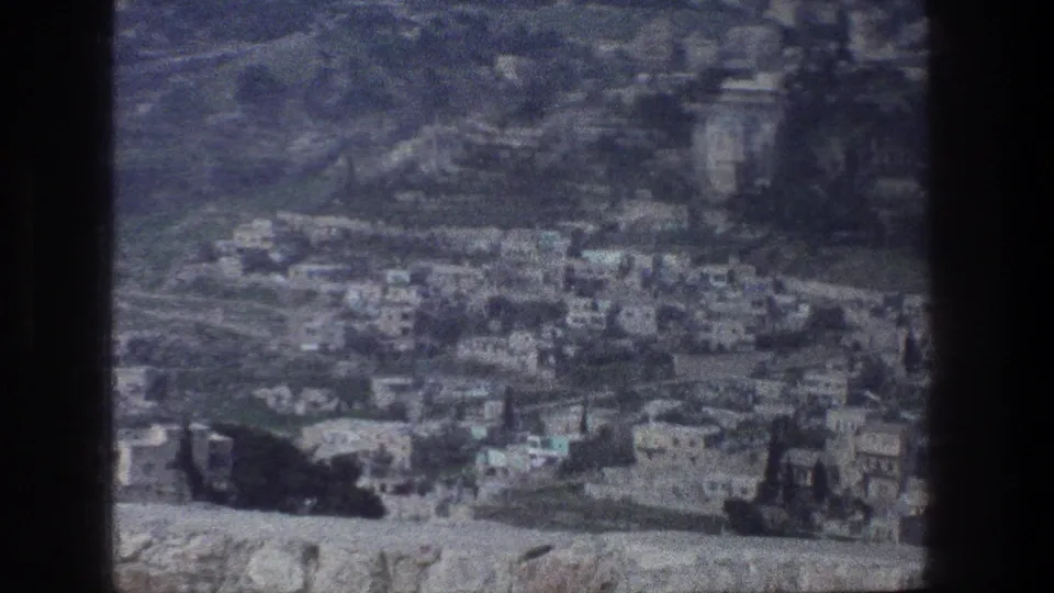 Elevated 1976 Jerusalem view showing dense hillside buildings, roads, and barren slopes in soft 8mm color.