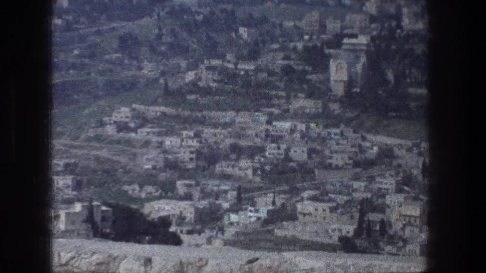 Jerusalem cityscape from an elevated visitor viewpoint, with clustered buildings and muted 1970s 8mm film texture.