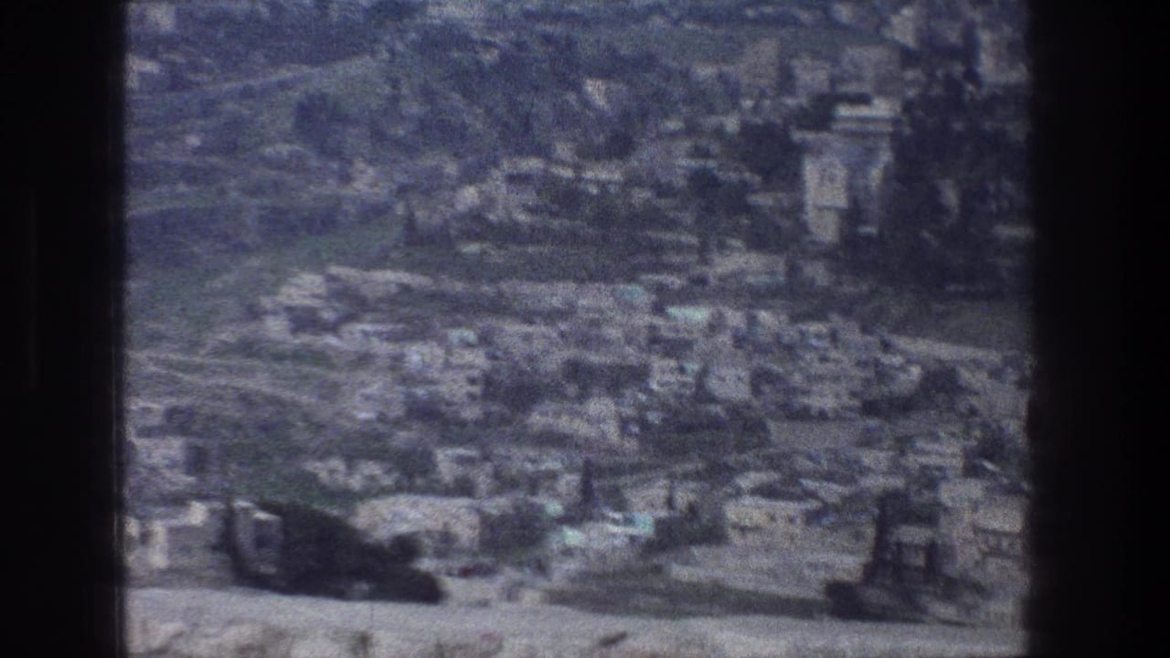 Soft aerial view of a dense hillside city with pale buildings and roads.