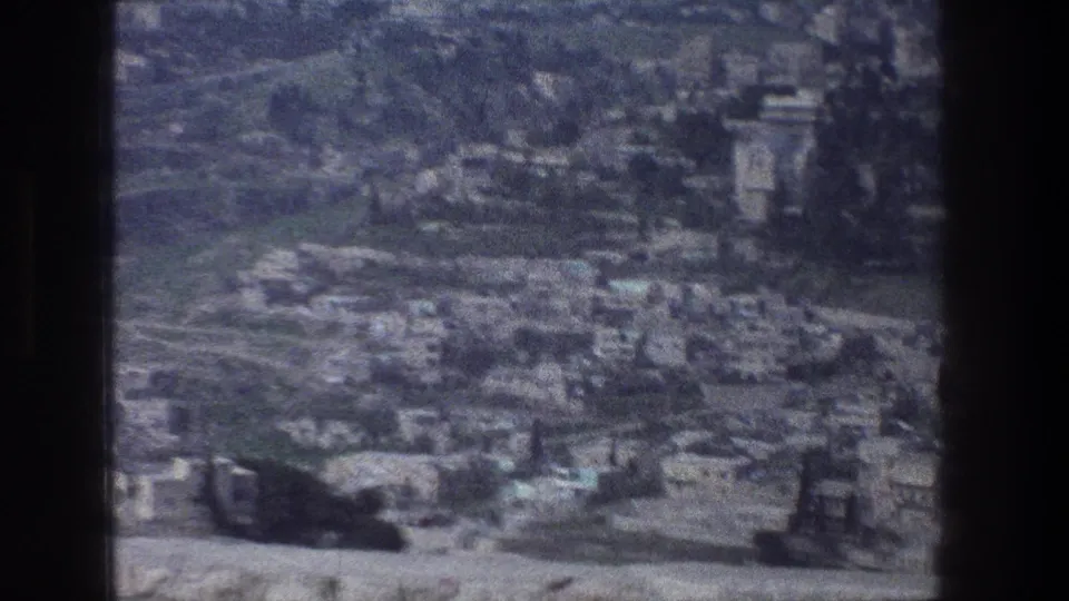 1976 8mm view over Jerusalem, showing dense pale buildings, hillside roads, greenery, and a dark film border.
