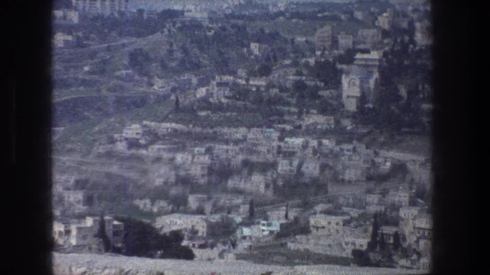 1976 Jerusalem cityscape from above, with clustered stone buildings, curved roads, greenery, and a tower-like landmark shape.