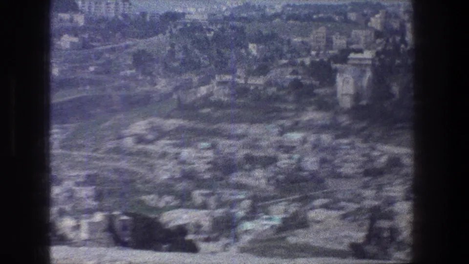Soft 1976 8mm frame of Jerusalem from above, showing dense hillside construction, roads, greenery, and contact-sheet borders.