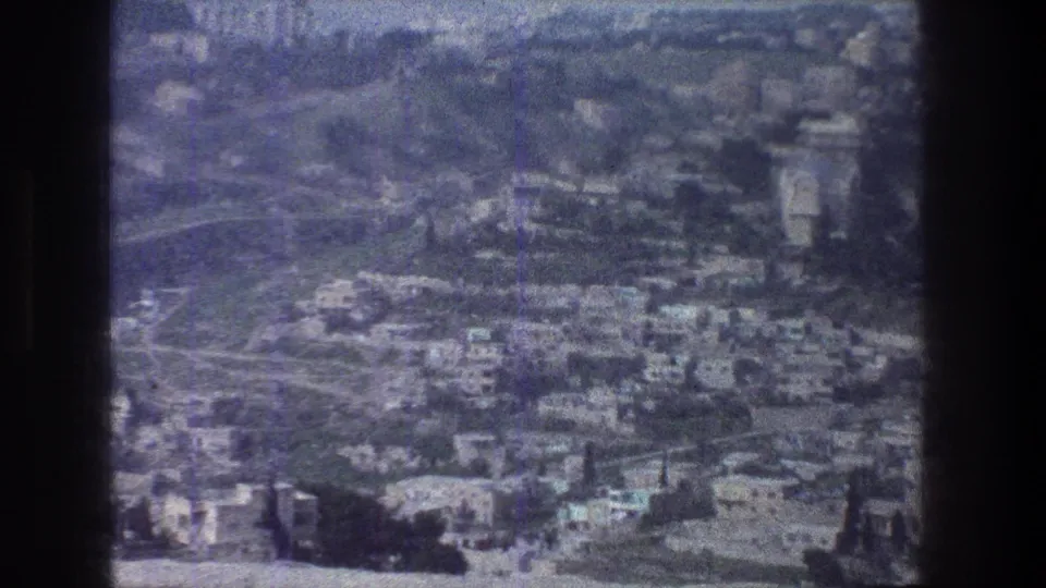Grainy 1976 Jerusalem aerial-style view with dense buildings, hillside roads, greenery, and visible film-frame vignetting.