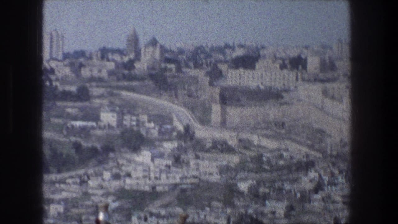 Jerusalem cityscape seen from above in 1976 8mm footage, with dense buildings, roads, and distant tower-like structures.