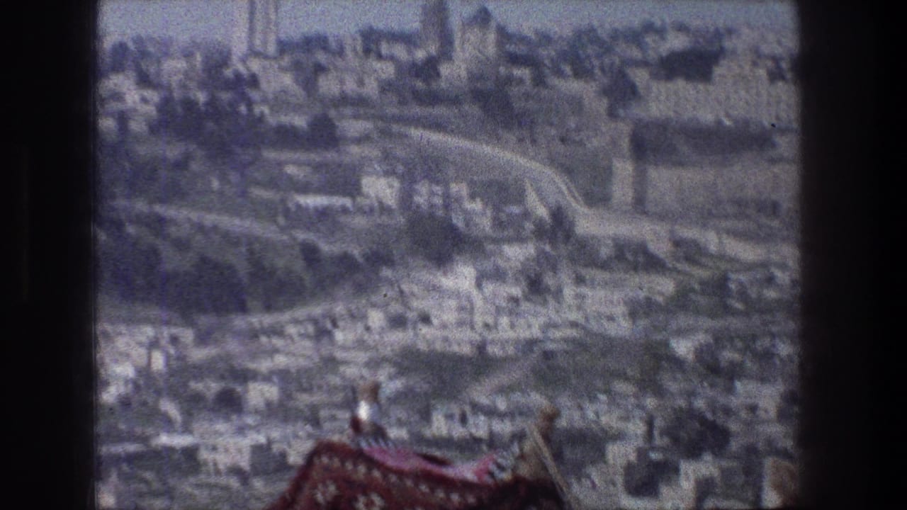 High vantage view of clustered buildings and roads, with a patterned textile at the lower edge.