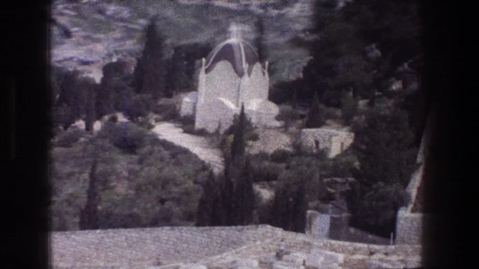 1976 8mm Jerusalem view of a white domed mausoleum or tomb set among cypress-like trees, shrubs, rocks, and stone paths.