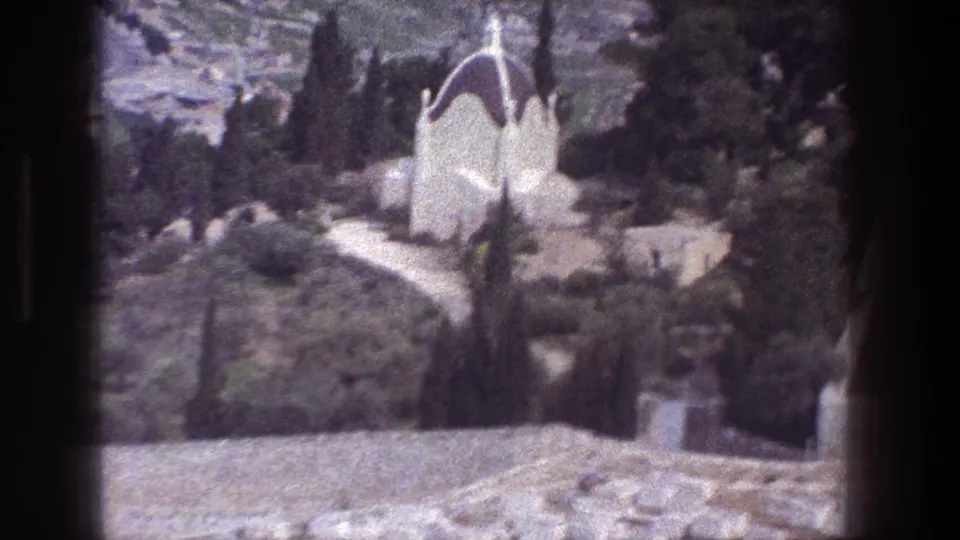 Soft 1976 8mm frame from Jerusalem, with a white domed tomb or mausoleum visible beyond cypress-like trees and stone paths.