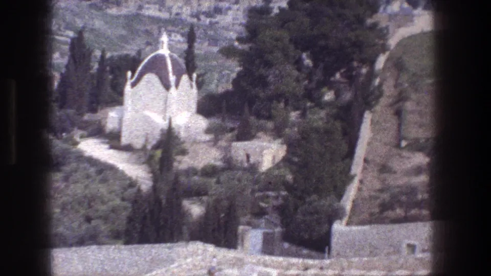 1976 8mm Jerusalem frame showing the white domed hillside structure partly framed by trees, rocks, walls, and a winding path.