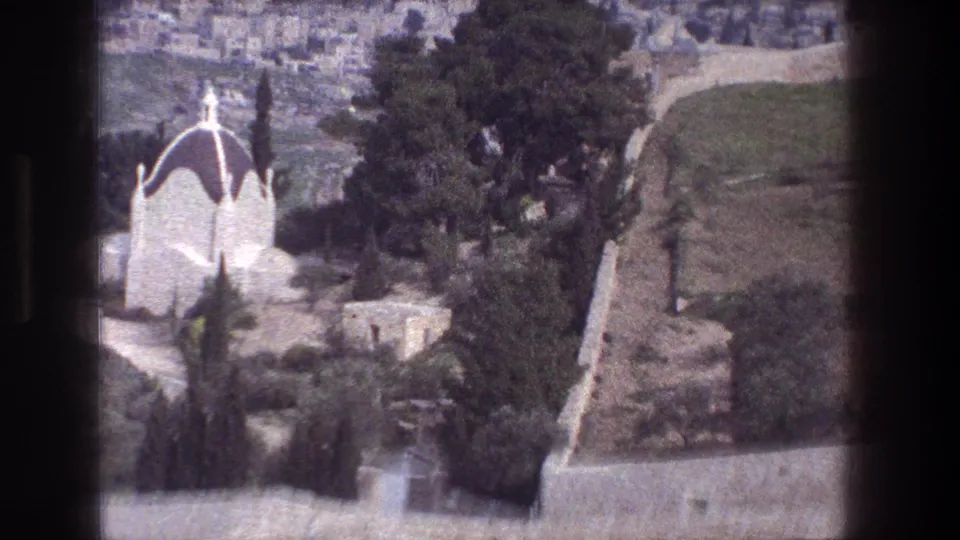 1976 Jerusalem 8mm frame showing a distant white domed building, cypress trees, stone walls, and hillside paths.