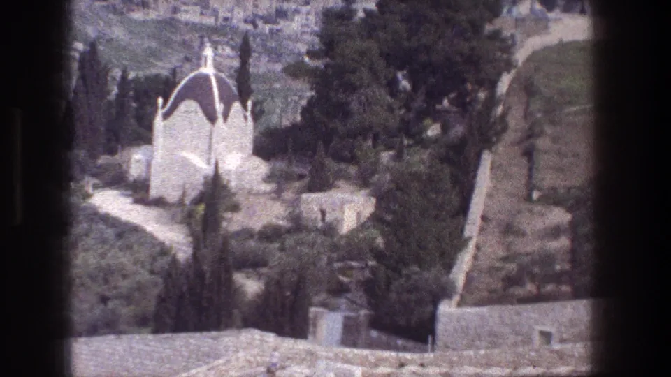 1976 Jerusalem view of a white domed building partly surrounded by trees, with stone paths and film-gate edges visible.