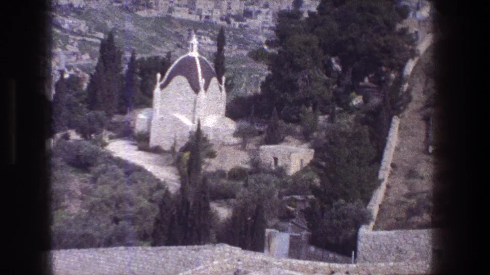 1976 Jerusalem 8mm still showing a white domed hillside building, surrounding trees, stone walls, and visible viewer-frame borders.