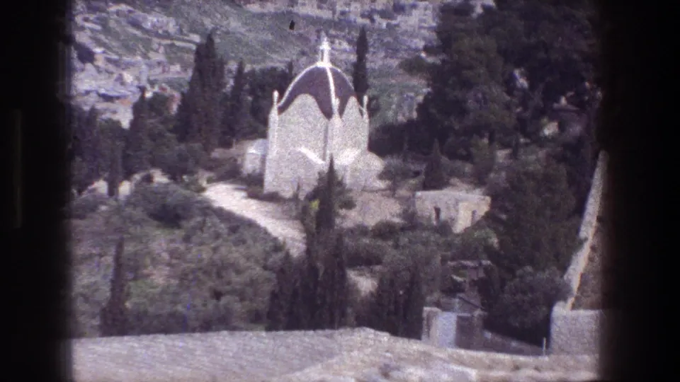 1976 8mm view from the Mount of Olives showing a white domed chapel, cypress trees, stone paths, and hillside terrain.