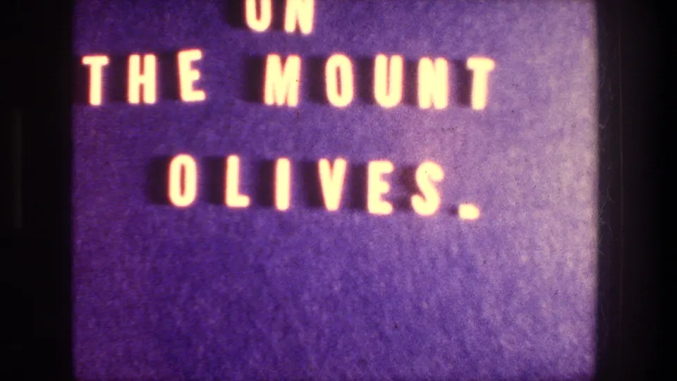 Blue 8mm title card with warm orange letters reading ON THE MOUNT OLIVES, identifying the Jerusalem overlook sequence.