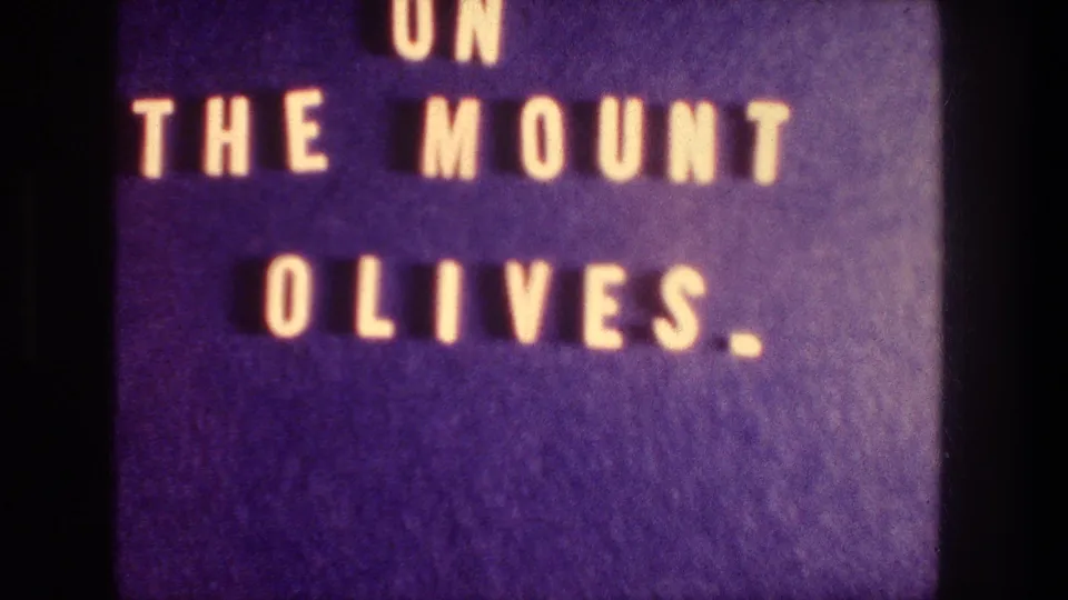 Second title-card frame from the 1976 8mm clip, showing the phrase ON THE MOUNT OLIVES against a blue background.