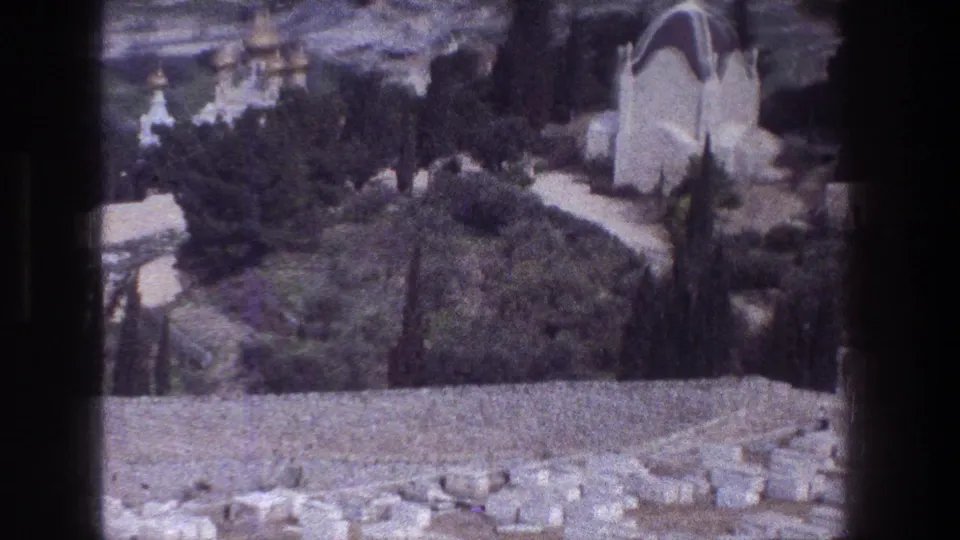 1976 8mm view from the Mount of Olives area showing trees, stone paths, and domed religious buildings in Jerusalem.