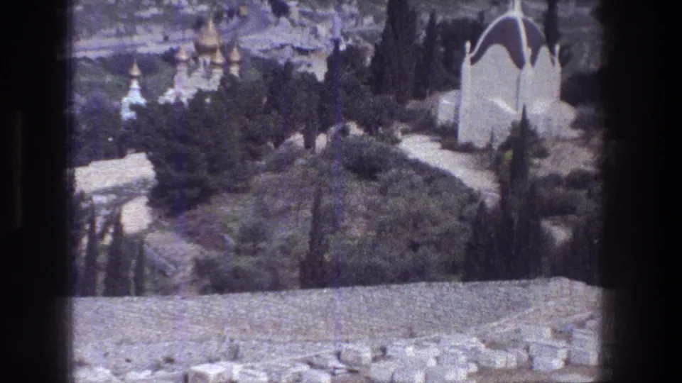 Soft 8mm Jerusalem view of the Mount of Olives area with cypress trees, walkways, and pale domed buildings.