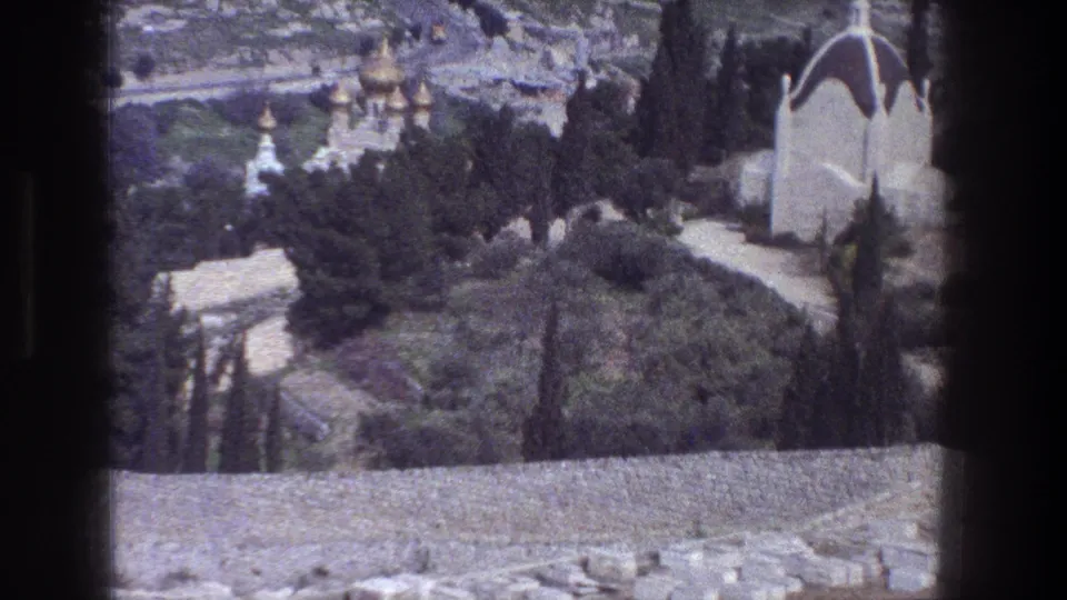 1976 8mm Jerusalem view from behind a stone wall, looking toward green trees, hillside paths, and distant church domes.