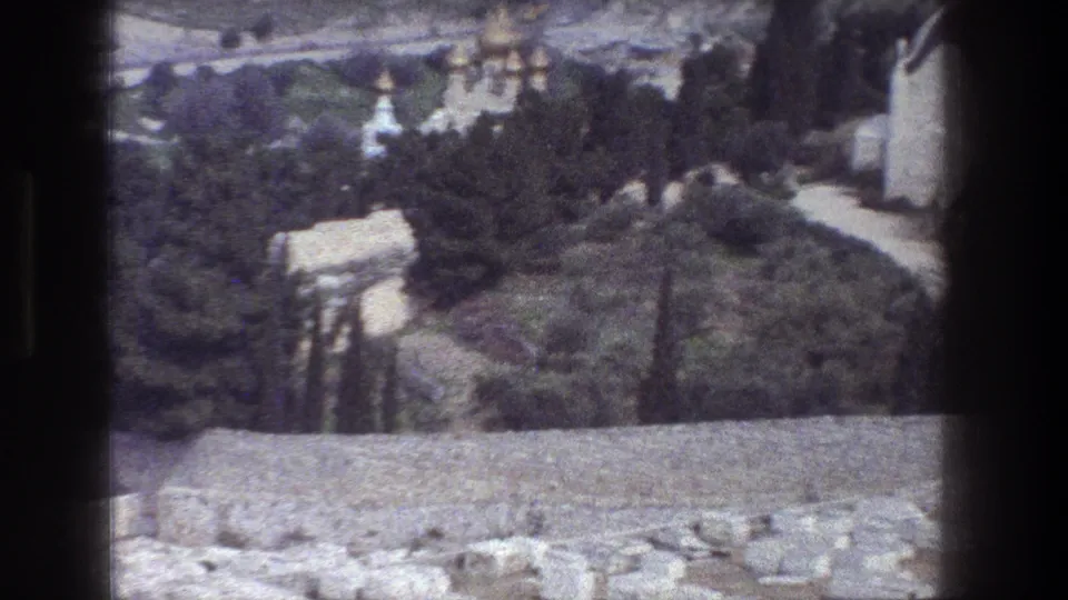 Soft, grainy 1976 8mm Jerusalem frame with stonework in front, trees below, paths, and distant religious domes.