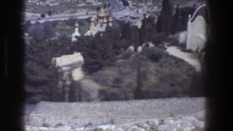 1976 8mm Jerusalem overlook showing a stone wall at the bottom, green trees, winding paths, and distant church domes.