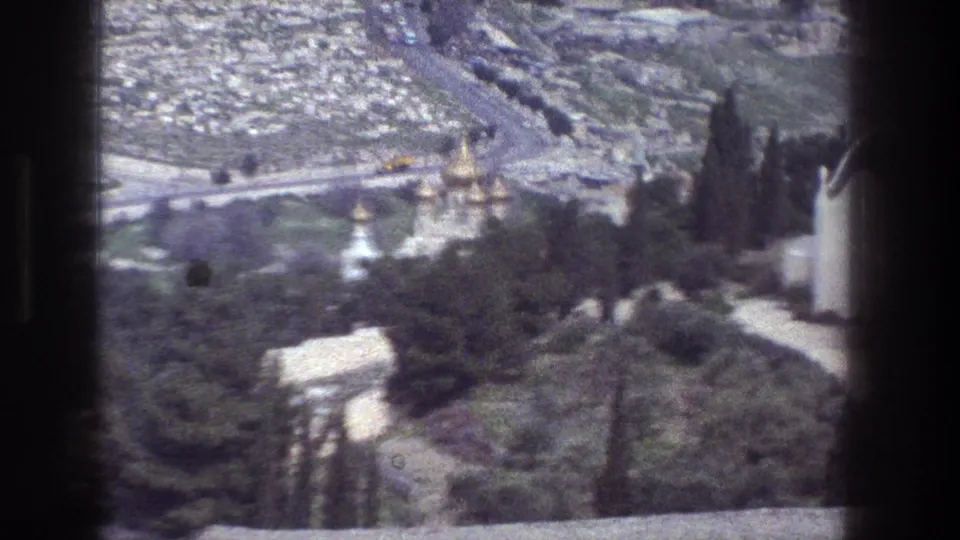 Jerusalem hillside view on 8mm film, with golden domes, a white tower, trees and a road crossing the background.