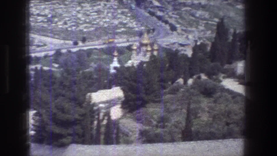 1976 Jerusalem overlook with soft-focus domed architecture, dark cypress-like trees, pale roofs and a road in the distance.