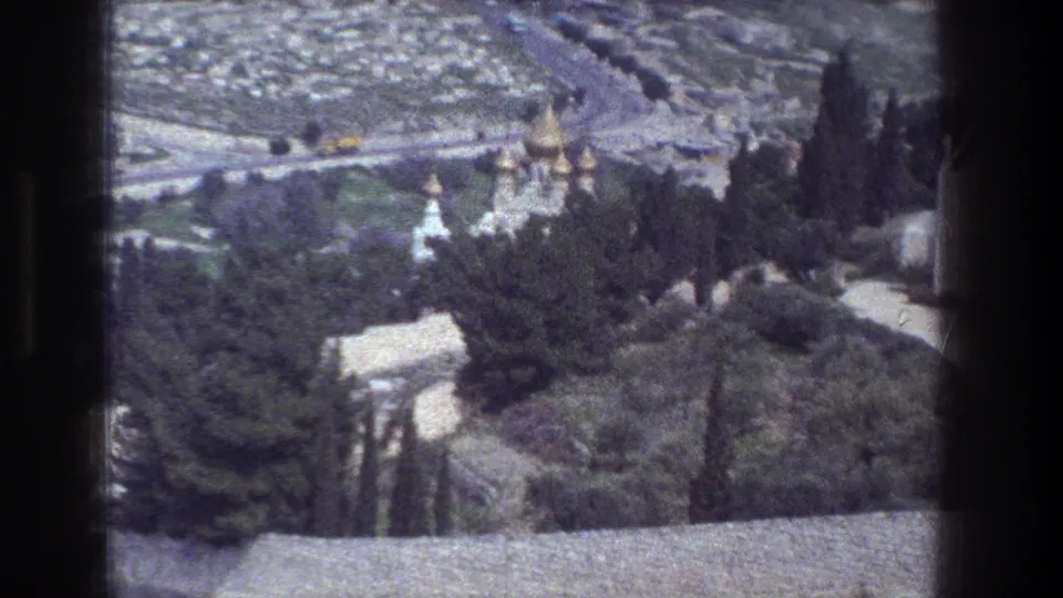 Jerusalem 8mm frame showing domed buildings and white towers among trees, with a road and hillside development beyond.