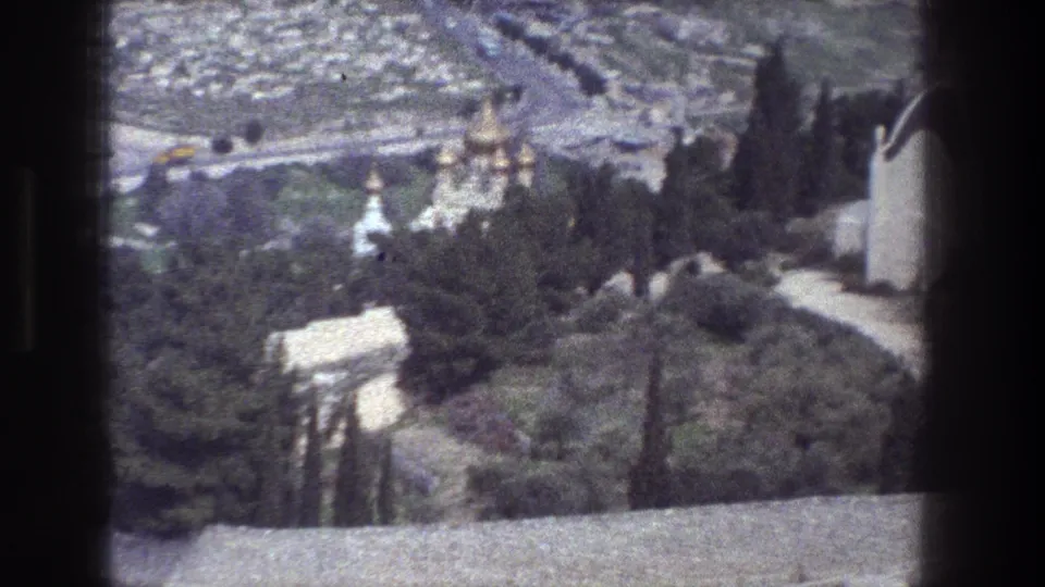 Soft 8mm frame of Jerusalem showing church domes among trees, roads and buildings beyond, and part of a white domed structure.
