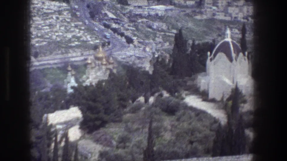 1976 Jerusalem home-movie frame with a white domed building in the foreground and gold church domes across the treed hillside.