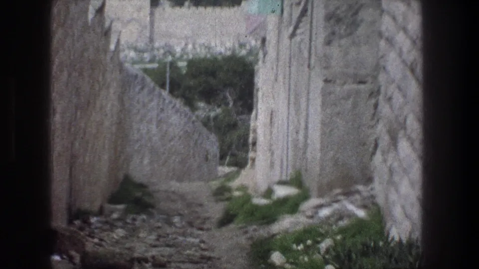 A handheld 8mm view of a Jerusalem stone passage, with steps, rough masonry walls, and greenery along the path.