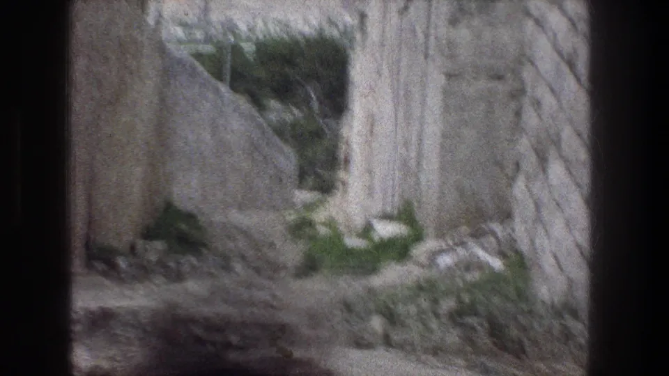 Soft, slightly blurred 1976 8mm frame of the inclined Jerusalem stone path, with walls, paving, rubble, and vegetation visible.