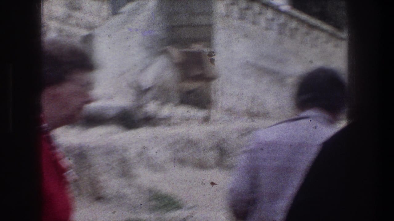 Blurred pedestrians pass in front of stone buildings and a donkey in the background.