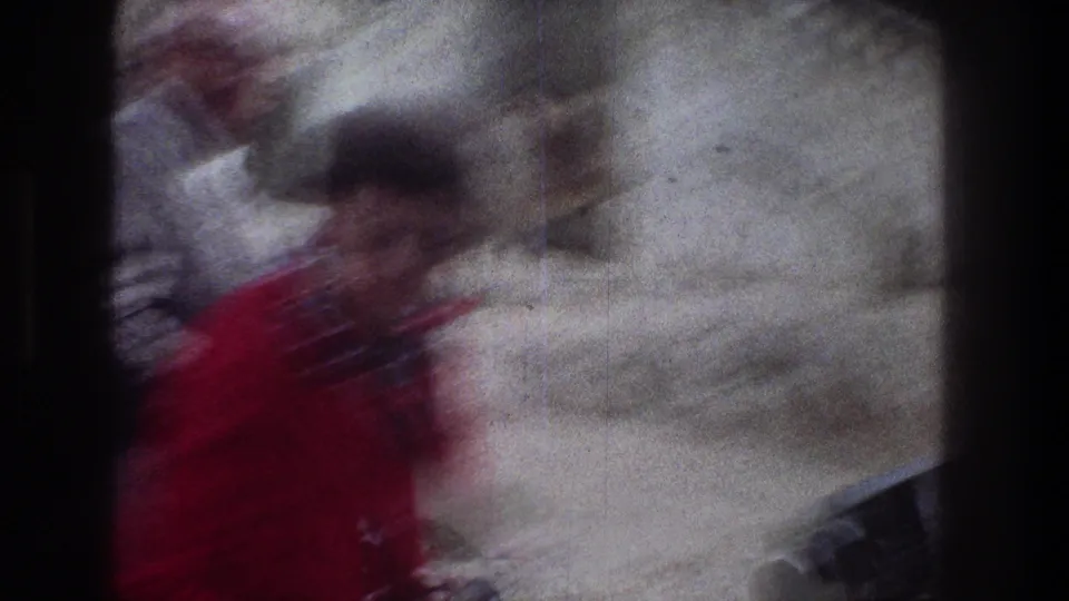 Soft, motion-blurred home-movie frame from Jerusalem showing a person in red passing close to the lens on a stone street.