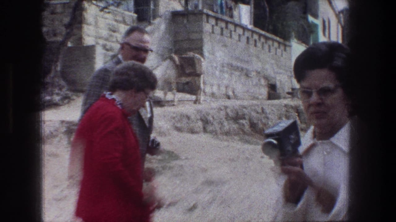 1976 Jerusalem home-movie frame showing tourists near stone walls at the Garden of Gethsemane, with one woman holding a small movie camera.