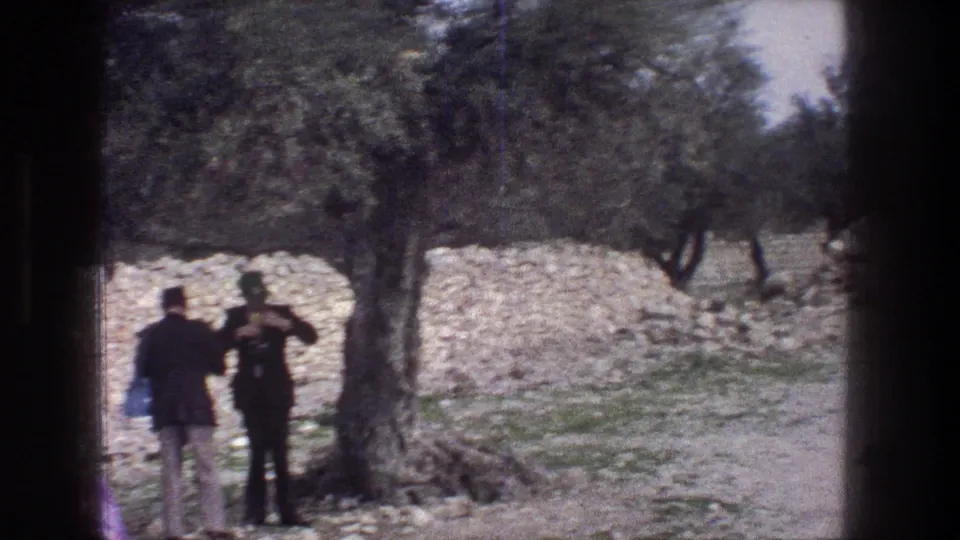 1976 Jerusalem frame with a man appearing to photograph the landscape beside another adult, olive trees, and a stone wall.