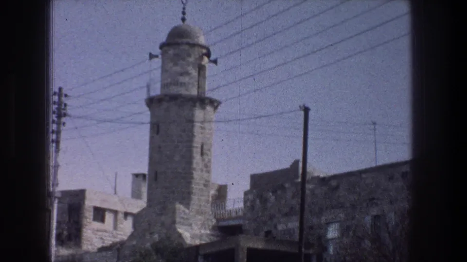 A stone minaret-like tower with a domed top rises above Jerusalem buildings, crossed by overhead power lines.