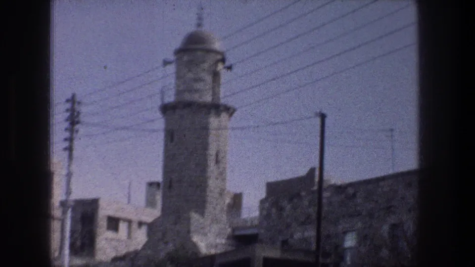 The Jerusalem tower remains centered with power lines, poles, rooftops, and stone building walls visible around it.