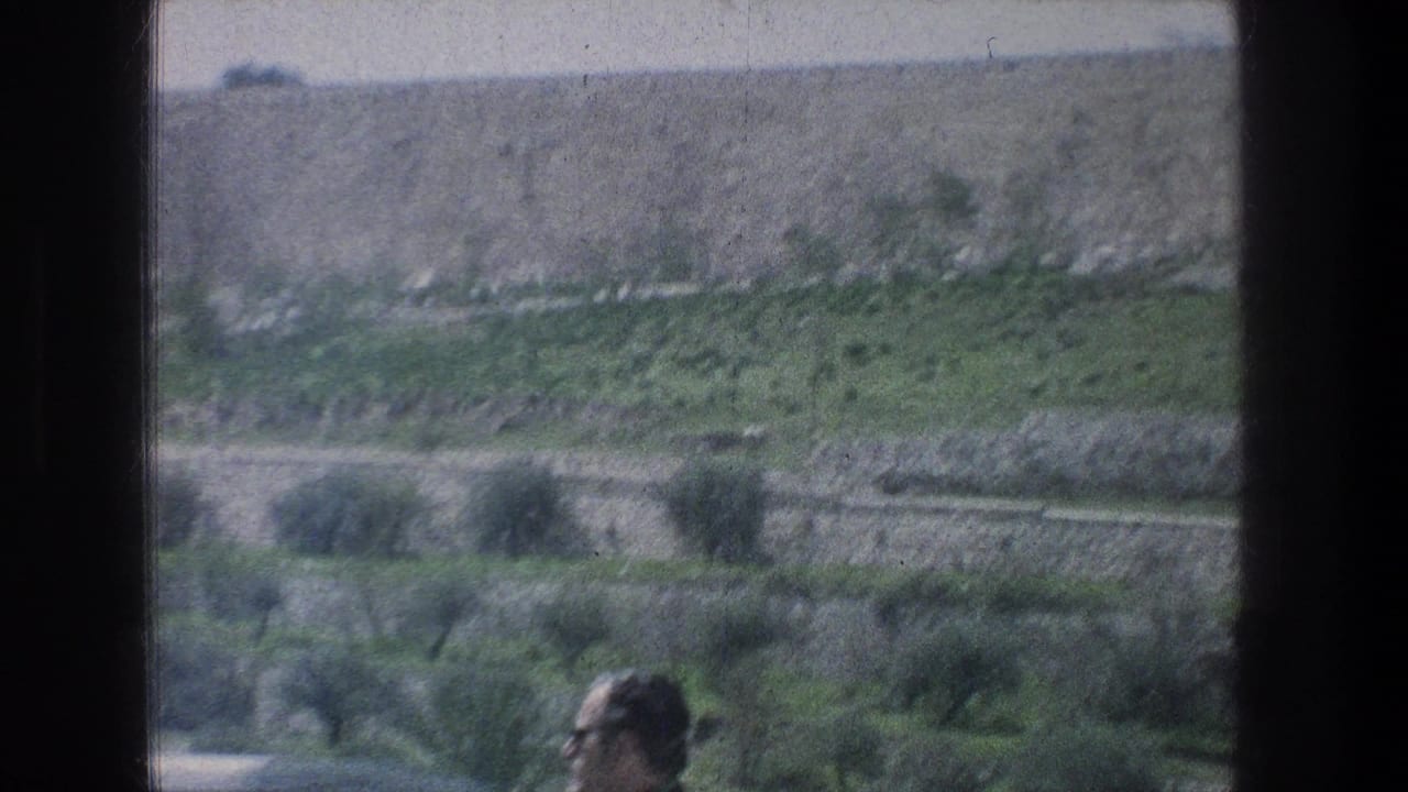 Terraced hillside and stone walls seen from a moving vehicle, with a blurred man at the bottom edge.