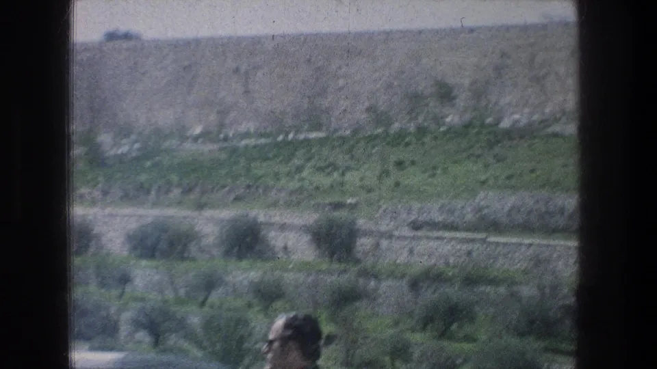 1976 Jerusalem roadside view of green terraces and stone retaining walls, with a partially visible passing man in the foreground.