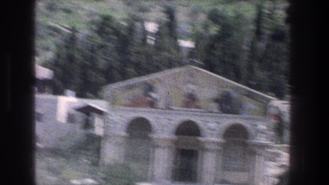 Blurred roadside view of the arched building and hillside trees through a dark window frame.